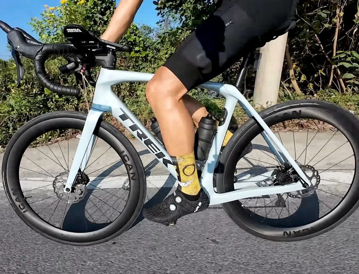 Close-up of cyclist pedaling on a Trek Domane SL5 fitted with ICAN AERO 50 II carbon wheels, ICAN rim decal visible, yellow socks and black cycling shoes