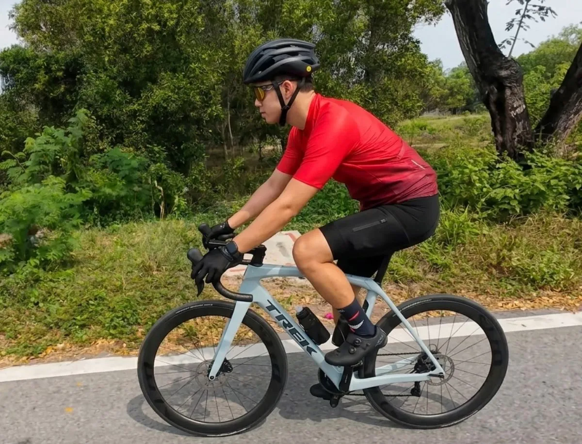 Mike Dee in red jersey and black bib shorts riding a light blue Trek Domane SL5 on a paved road during carbon wheel climbing performance test