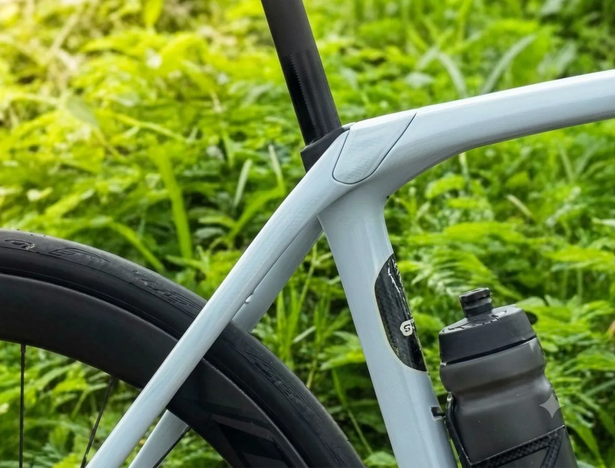Trek Domane SL5 IsoSpeed decoupler junction showing seat tube flex point where it separates from the top tube on OCLV carbon frame in Plasma Grey Pearl, shot outdoors against green foliage