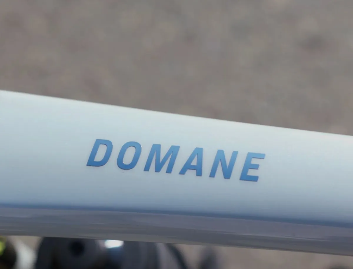 Close-up of Domane lettering decal in gradient blue on Trek OCLV carbon frame top tube in Plasma Grey Pearl finish