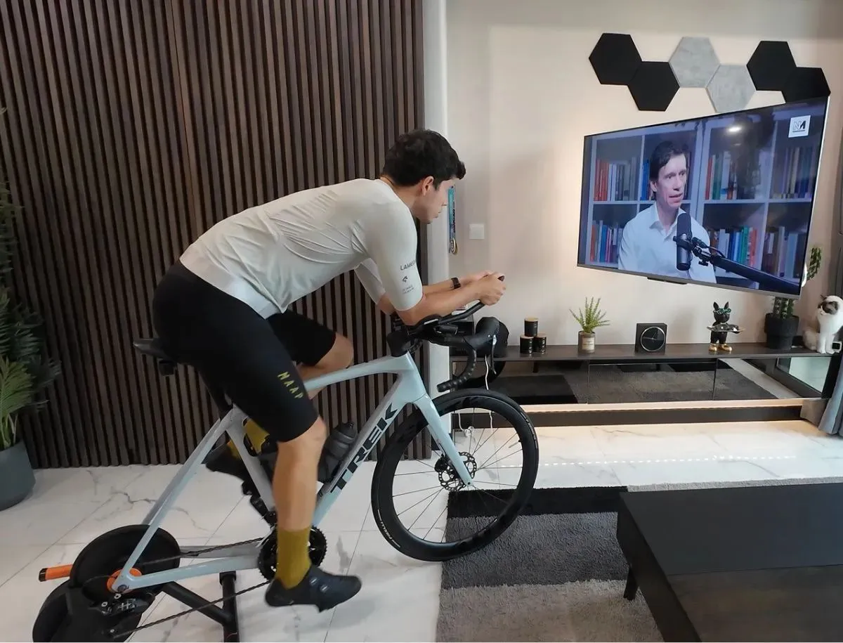 Mike Dee riding a Trek Domane SL5 road bike on an indoor smart trainer, wearing a white LAMEDA cycling jersey and black bib shorts, testing Chinese cycling apparel comfort during an extended session for BikeLabHQ.