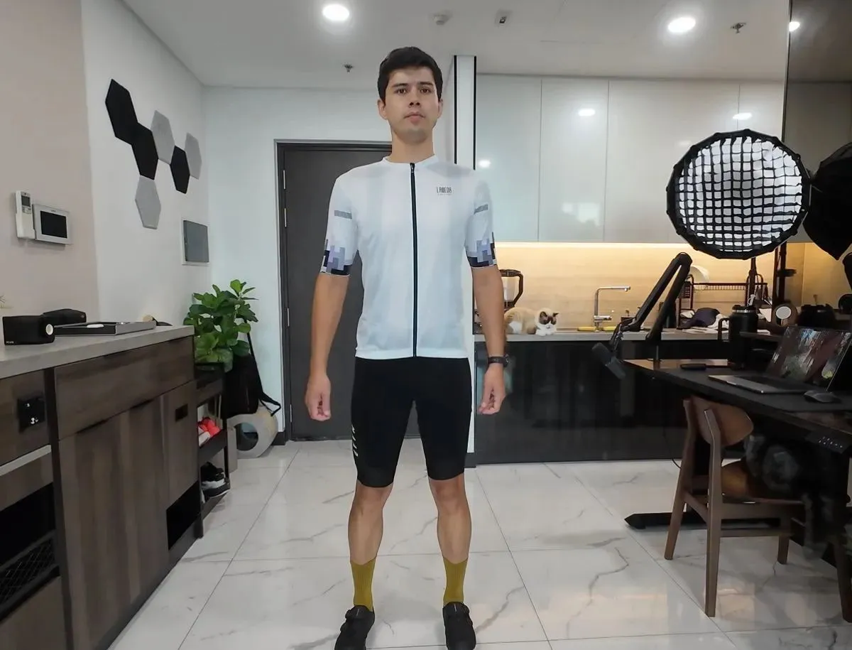 Mike Dee wearing a white LAMEDA men's cycling jersey with black bib shorts and mustard socks in a home studio, showing fit and fabric finish for this BikeLabHQ Chinese cycling apparel review.