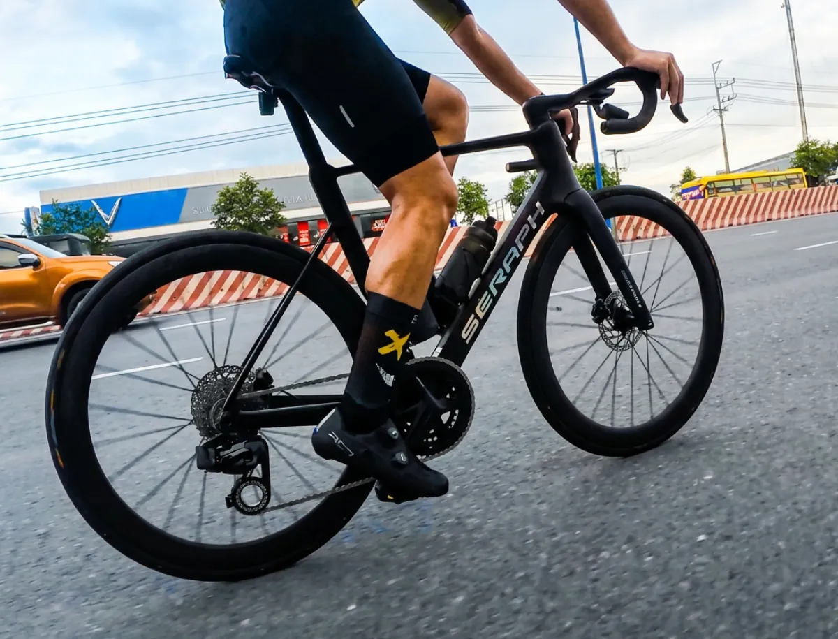 Mike Dee riding the Seraph TT-X71 carbon road bike in traffic, showing the drivetrain and cassette in motion