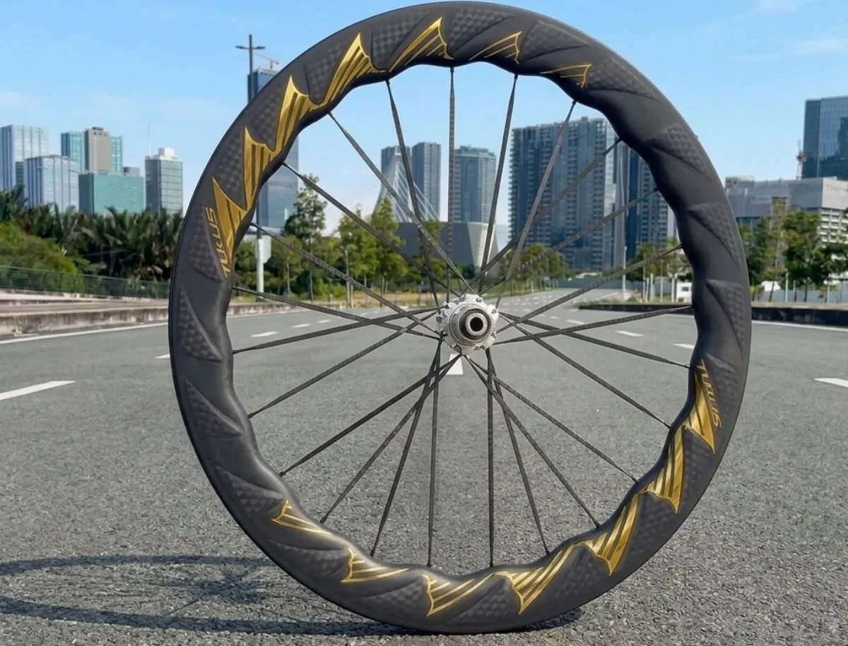 Full view of TUKUS Bluefin Turbo SR carbon wheel with wave rim, gold fin graphics, and city skyline background