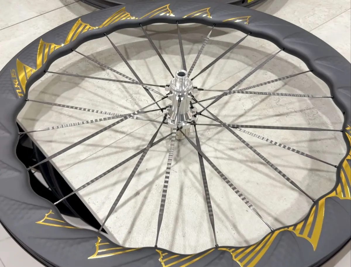 Overhead view of TUKUS Bluefin Turbo SR wheel showing wide flat carbon spoke blades laced from hub to gold fin rim