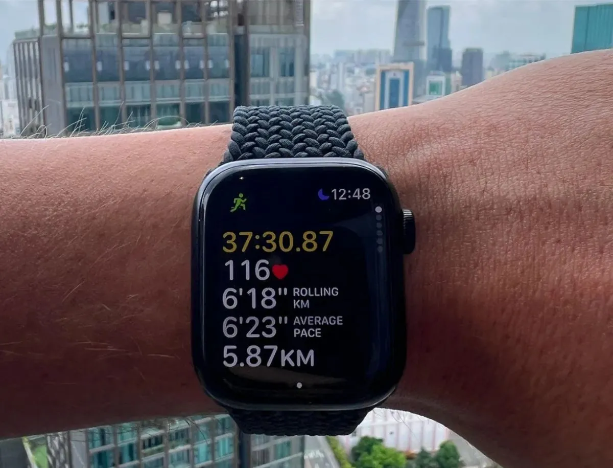 Apple Watch worn on wrist during an outdoor run in an urban setting, showing elapsed time of 37:30.87, heart rate of 116 BPM, rolling pace of 6'18" per km, and average pace of 6'23".