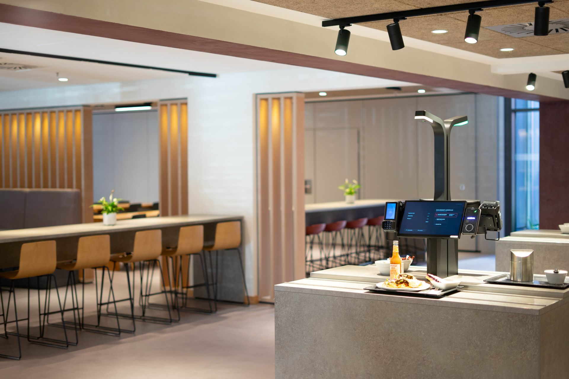 Modern dining area with wooden chairs and tables, and a self-service kiosk with food tray.