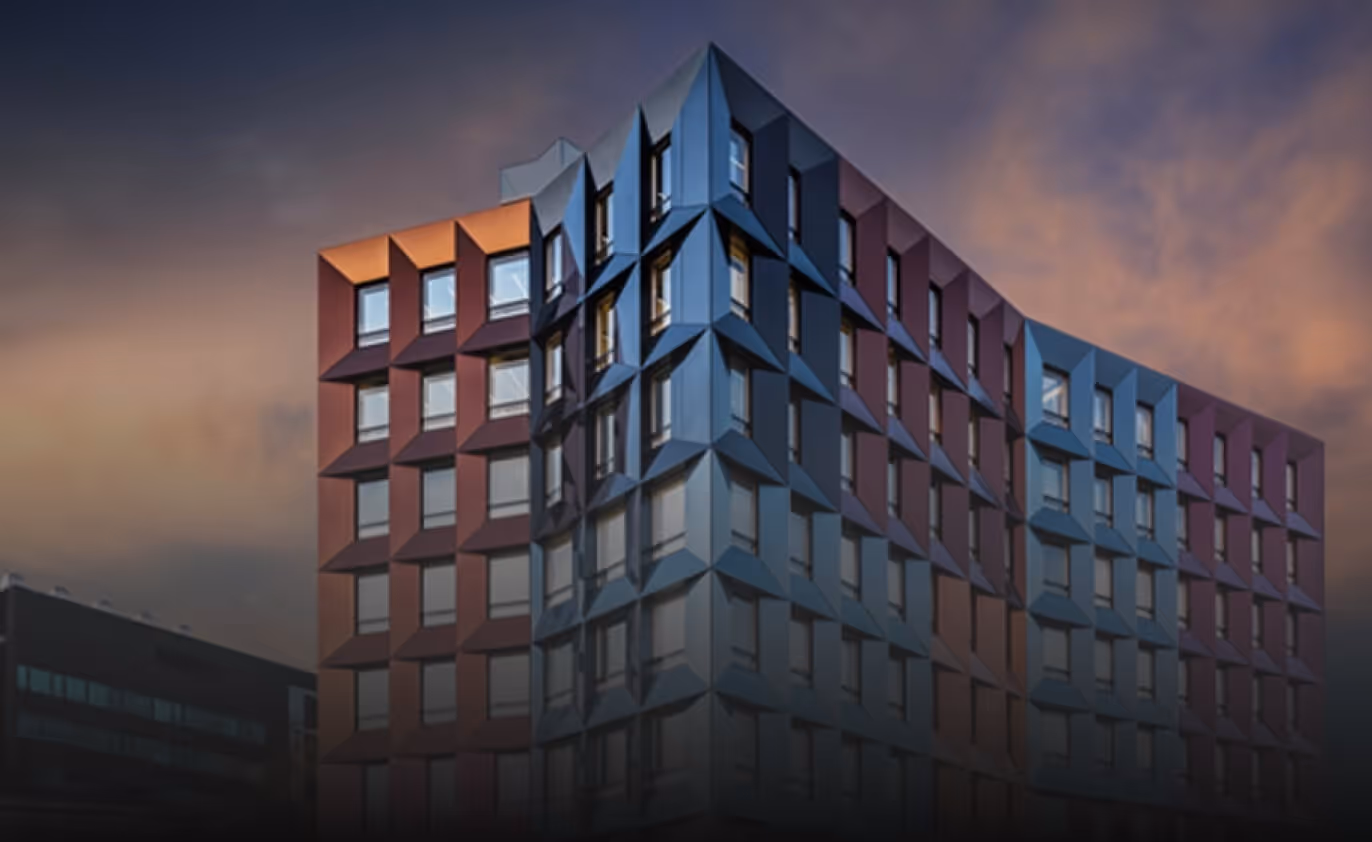Modern multi-story building featuring an intricate, multi-colored geometric facade made from Euramax coated aluminium panels under a sunset sky.