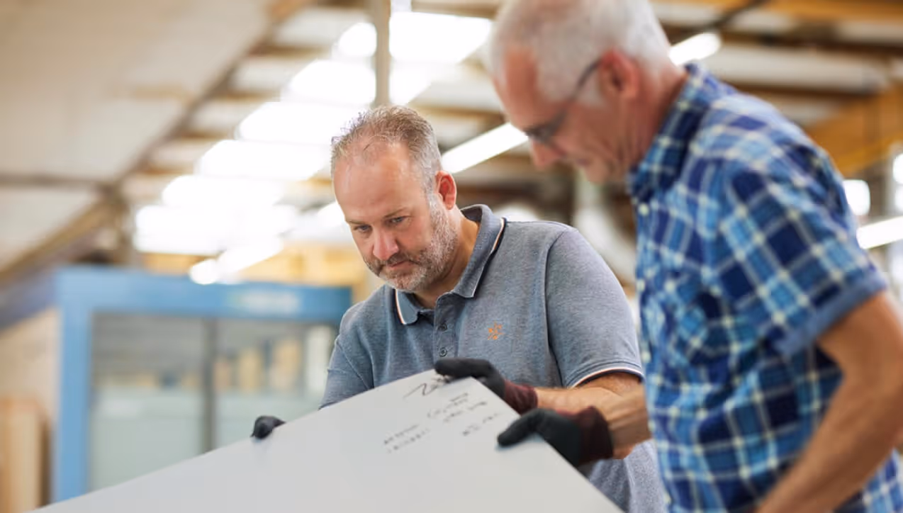 Two Euramax quality assurance technicians inspecting a coated aluminium metal cladding sheet in a factory production setting.