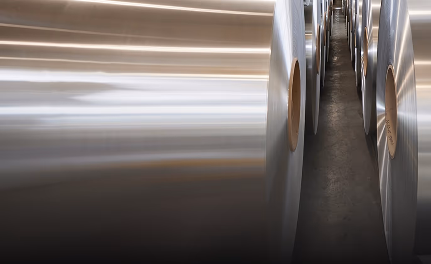Rows of large, reflective coated aluminium coils stored inside a Euramax manufacturing warehouse facility.