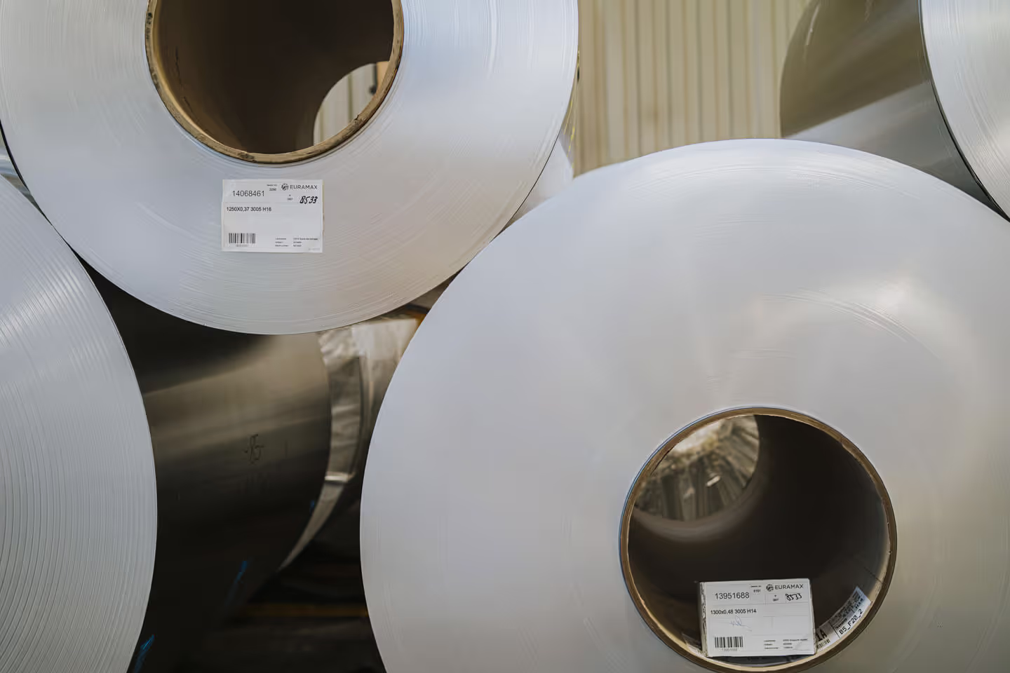 Stacked rolls of eco-friendly, zero-carbon raw aluminium coils with official Euramax factory tracking labels inside a storage warehouse.