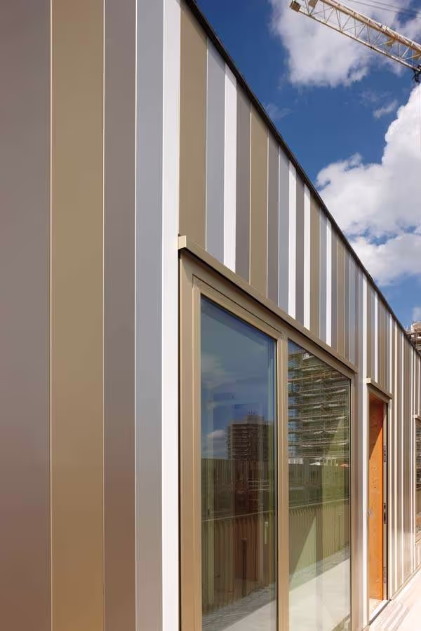 Close-up view of a building facade clad in vertical neutral-toned Anomax anodized aluminium strips by Euramax, reflecting the surrounding cityscape.