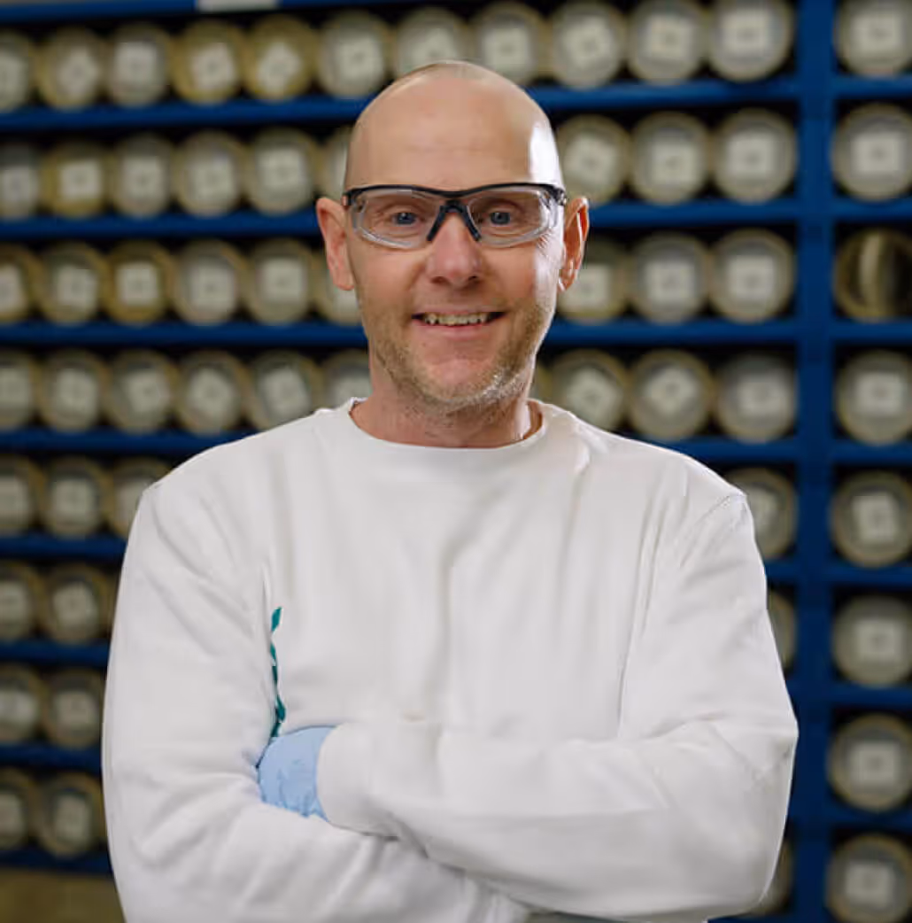 Portrait of a Euramax factory specialist wearing safety glasses and protective gear, standing in front of a manufacturing storage rack.