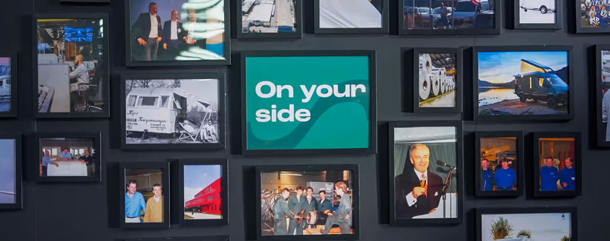 A corporate gallery wall of framed legacy photos centered around a green sign that reads On Your Side, reflecting Euramax company values.