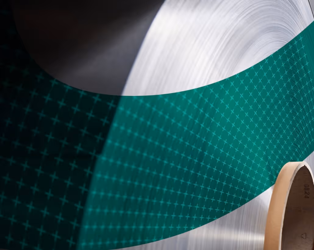 A detailed close-up of a gleaming silver raw aluminium coil with a green geometric patterned overlay, highlighting Euramax’s precision metal coating process.