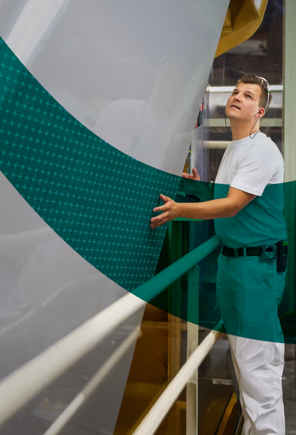 A factory worker checking a wide sheet of pre-coated aluminium during the manufacturing and quality control process.
