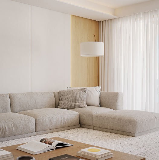 Divano angolare beige con cuscini in salotto luminoso con lampada e tende bianche.