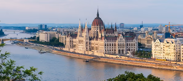 View of Budapest Parliament building by the Danube River with cityscape in the background.