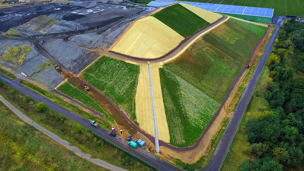 Aerial view of a large farmland divided into irregular green and yellow plots with construction vehicles nearby.