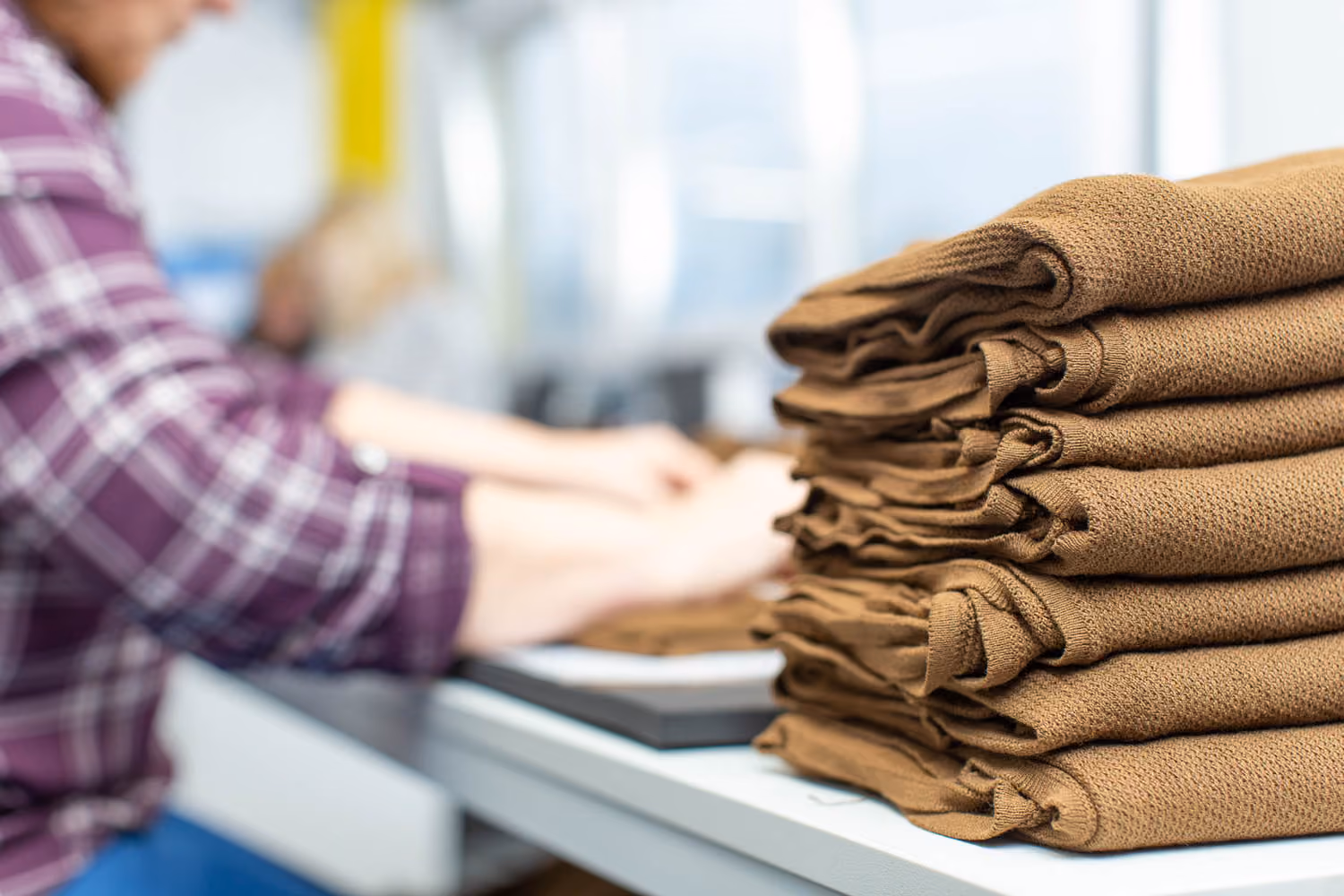 Mitarbeiterin stapelt gefaltete Tarnbekleidung in der Produktion.