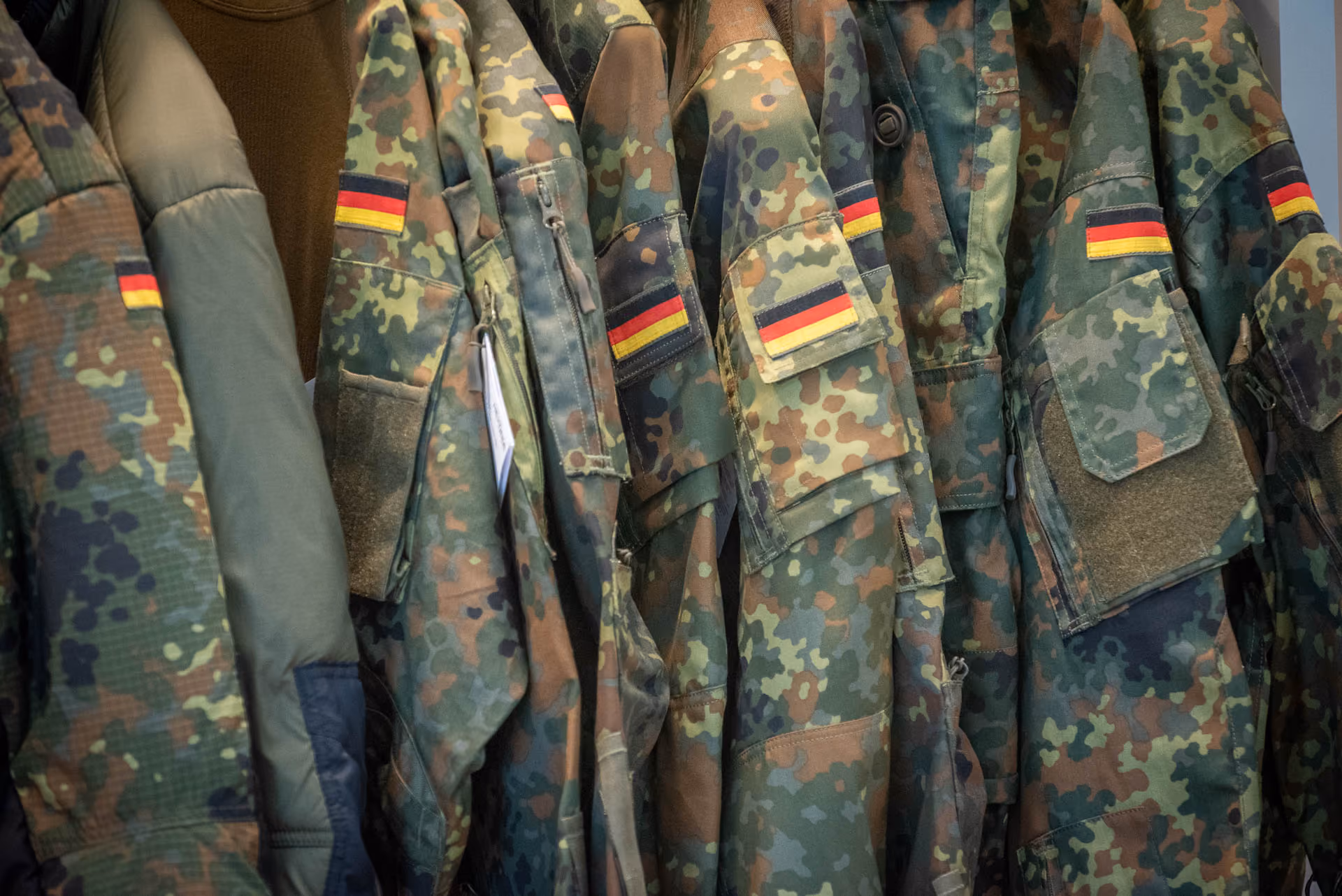 Tarnuniformen mit deutschen Flaggen hängen nebeneinander.