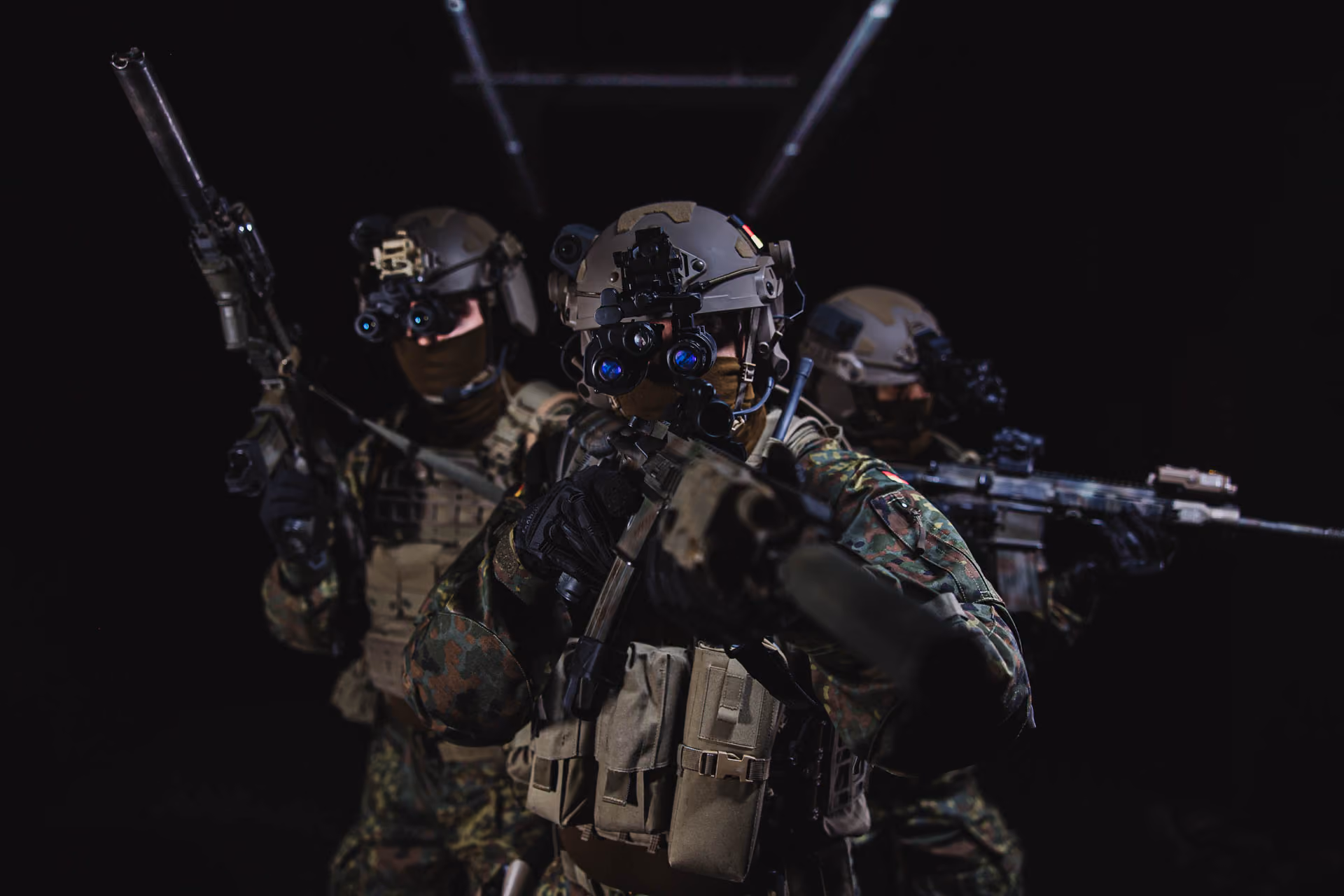 Soldaten mit Gefechtshelmen, Nachtsichtgeräten und Gewehren in dunkler Umgebung.