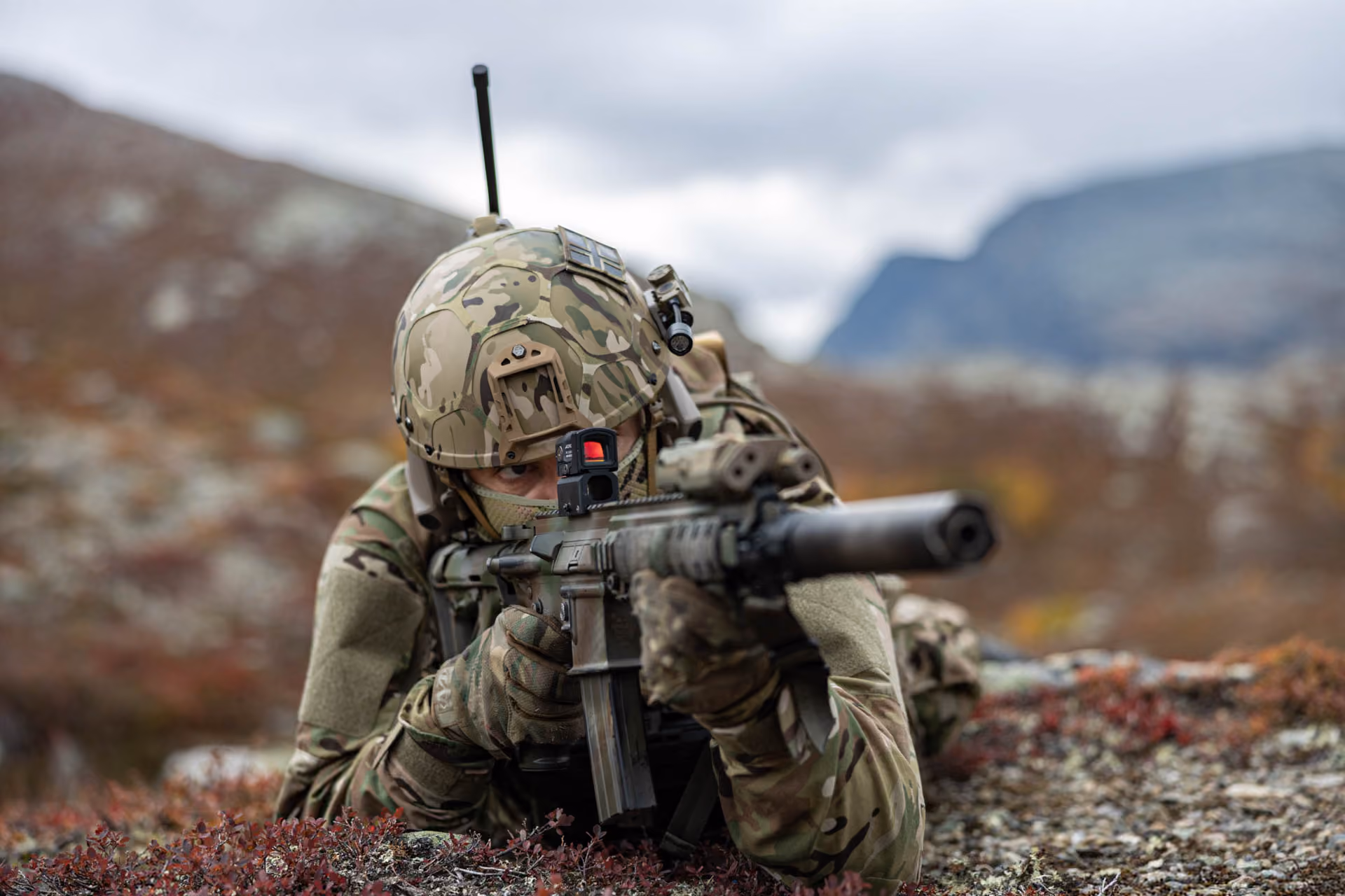 Soldat mit Gefechtshelm zielt liegend in einer Berglandschaft.
