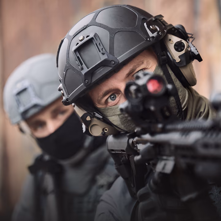 Zwei Einsatzkräfte mit Gefechtshelmen zielen aus der Deckung mit Gewehren.