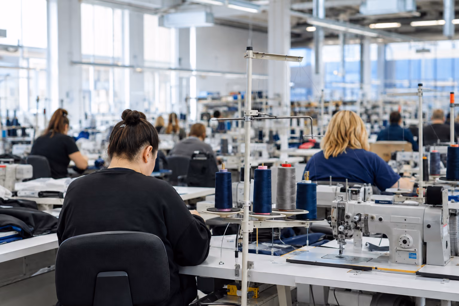 Mitarbeitende arbeiten an Nähmaschinen in einer modernen Textilproduktion.