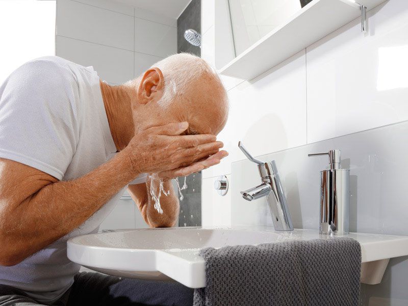 Ein Mann, der sich in einem barrierereduzierten Waschbecken das Gesicht wäscht.