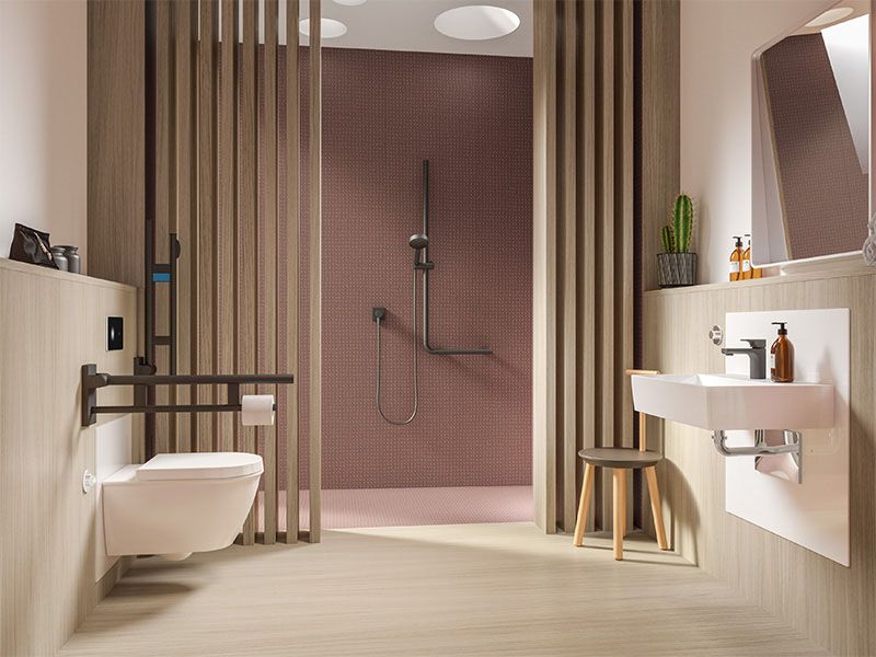 Ein Badezimmer mit einem barrierereduzierten WC mit Stütze, einer großen, bodenebenen Dusche mit Duschreling und einem unterfahrbaren Waschtisch.