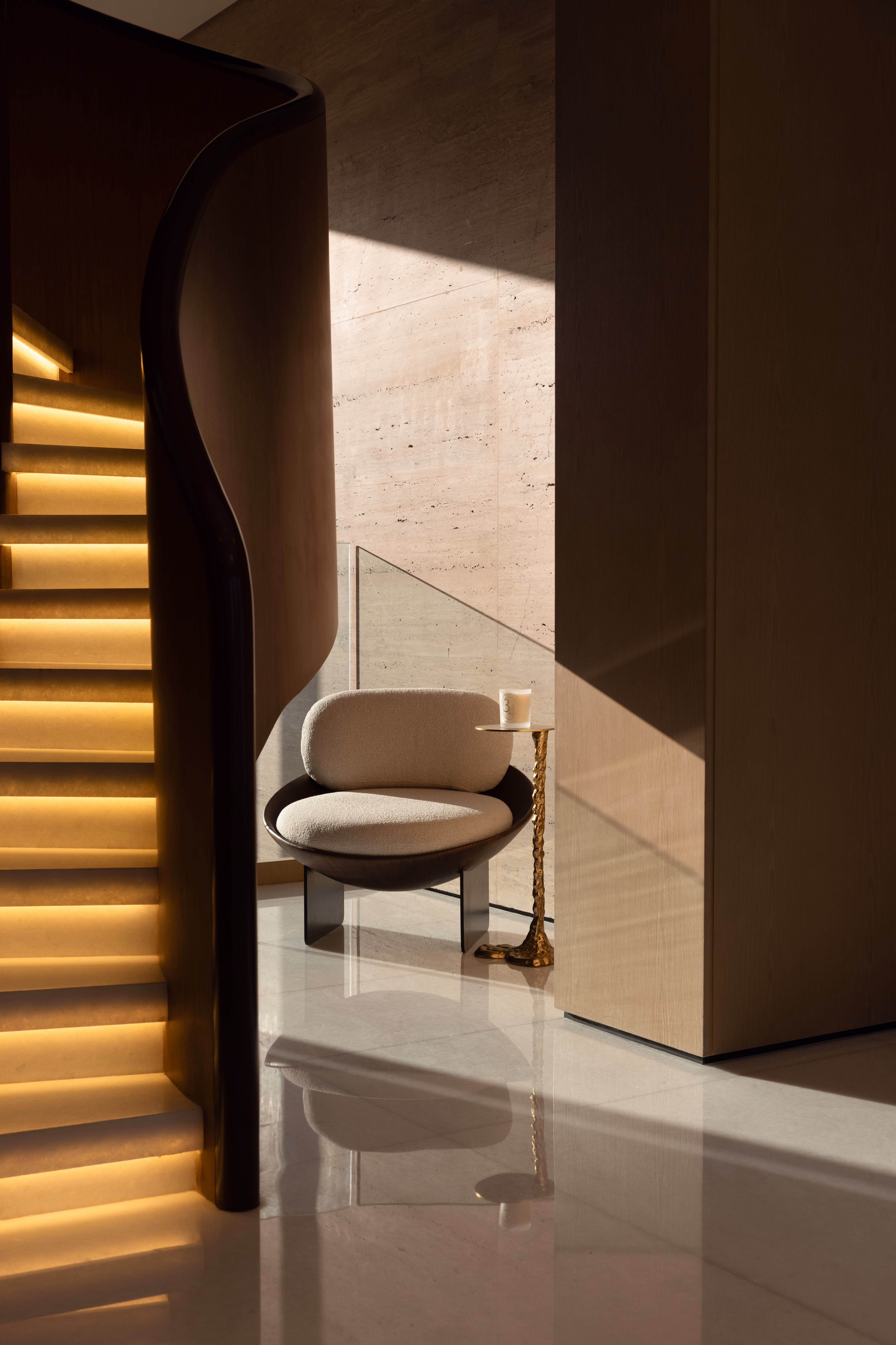 Interior hallway with sculptural staircase and designer chair by Emkaan