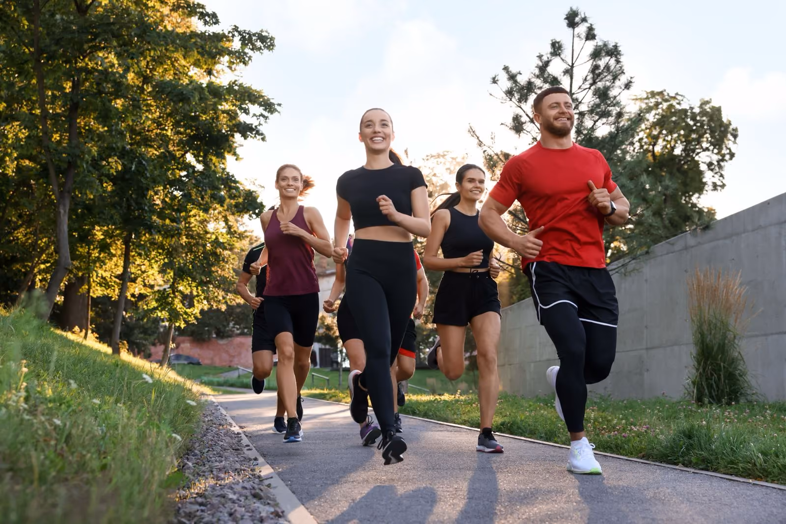 Een groep van zes jonge mensen jogging buiten op een pad omringd door bomen en gras.