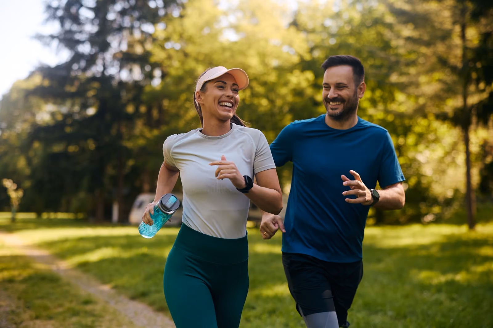 Vrolijk stel joggend op een bospad in sportkleding op een zonnige dag.