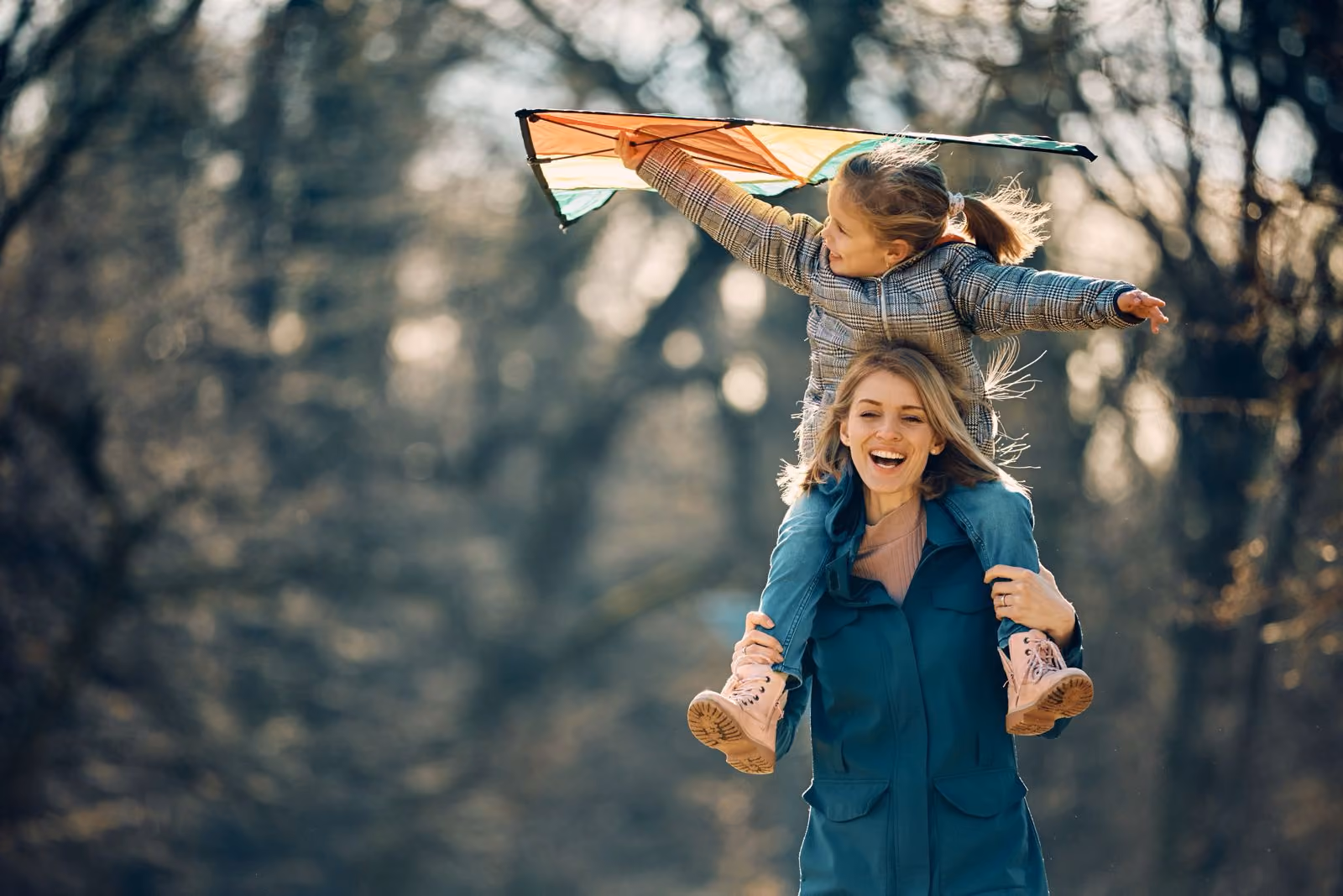 Vrouw die een lachende kind op haar schouders draagt terwijl het een vlieger vasthoudt in een park.