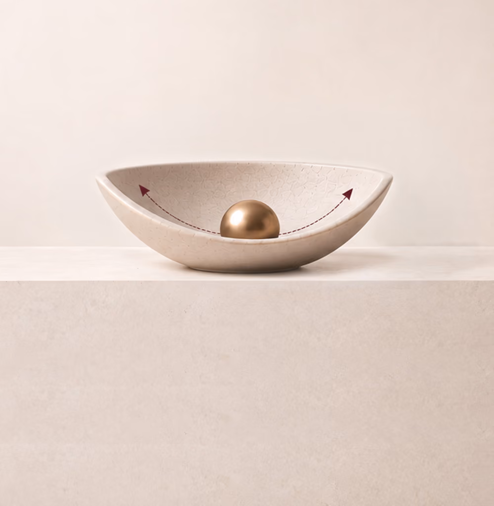 Schotelvormige keramische kom met een gouden bol in het midden en pijlen die van de bol naar de randen wijzen, geplaatst op een beige oppervlak tegen een lichte achtergrond.