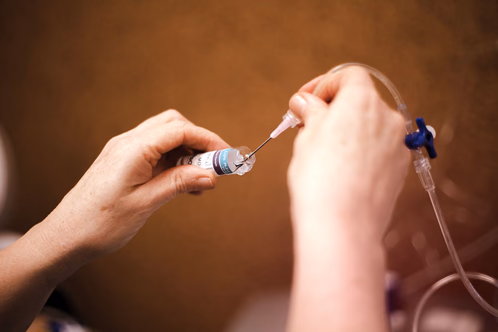 Een persoon trekt vloeistof met een injectienaald uit een flesje voor medicatie.