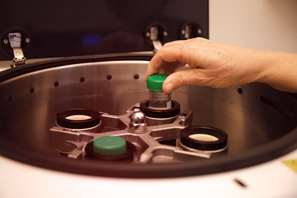Hand placing a small tube with a green cap into a laboratory centrifuge machine.