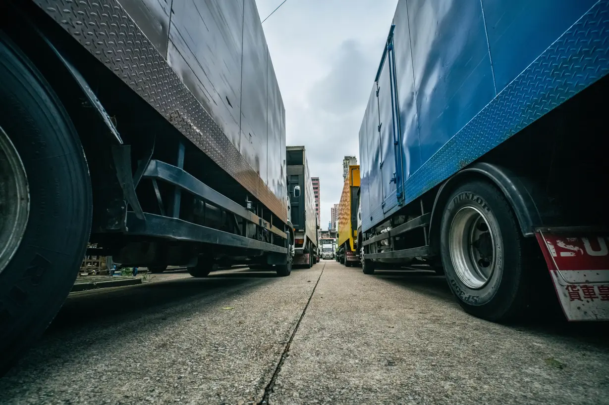 Low-angle view of commercial freight trucks parked on either side of a road in an urban area.