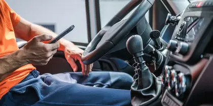 Truck driver using a mobile phone inside the vehicle's cabin near the steering wheel.