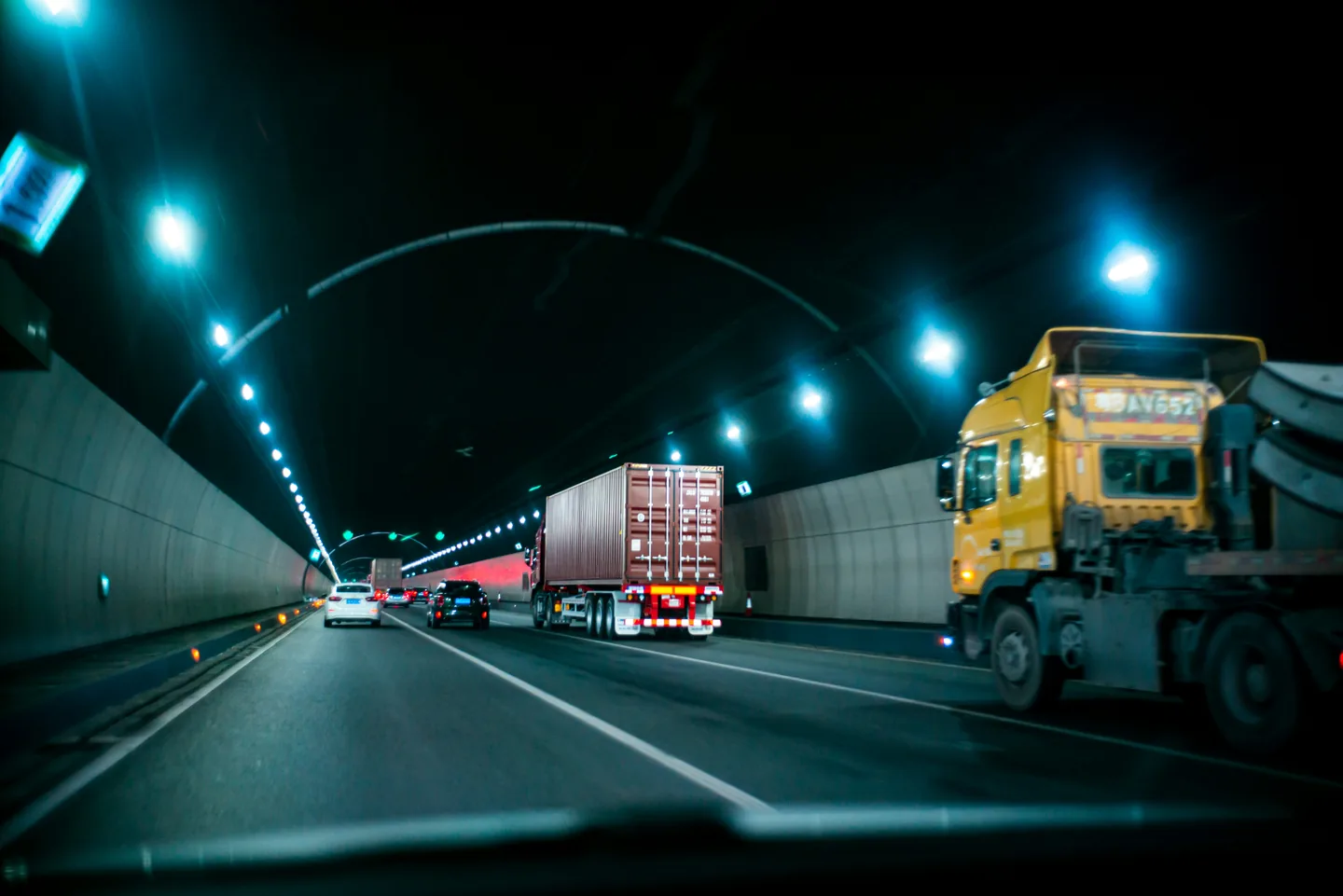 Traffic including trucks and cars moving through a lit road tunnel at night.