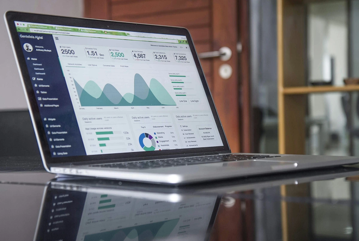 Open laptop on a reflective surface displaying data analytics dashboards with charts and graphs.