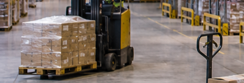 Forklift moving stacked pallets wrapped in plastic in a large warehouse with concrete floor.