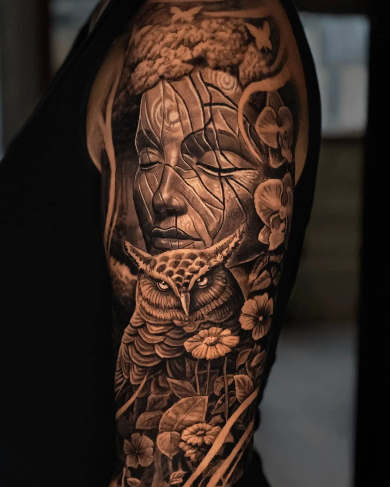 Realistisk overarms-tatovering med ugle, blomster og et roligt stenansigt