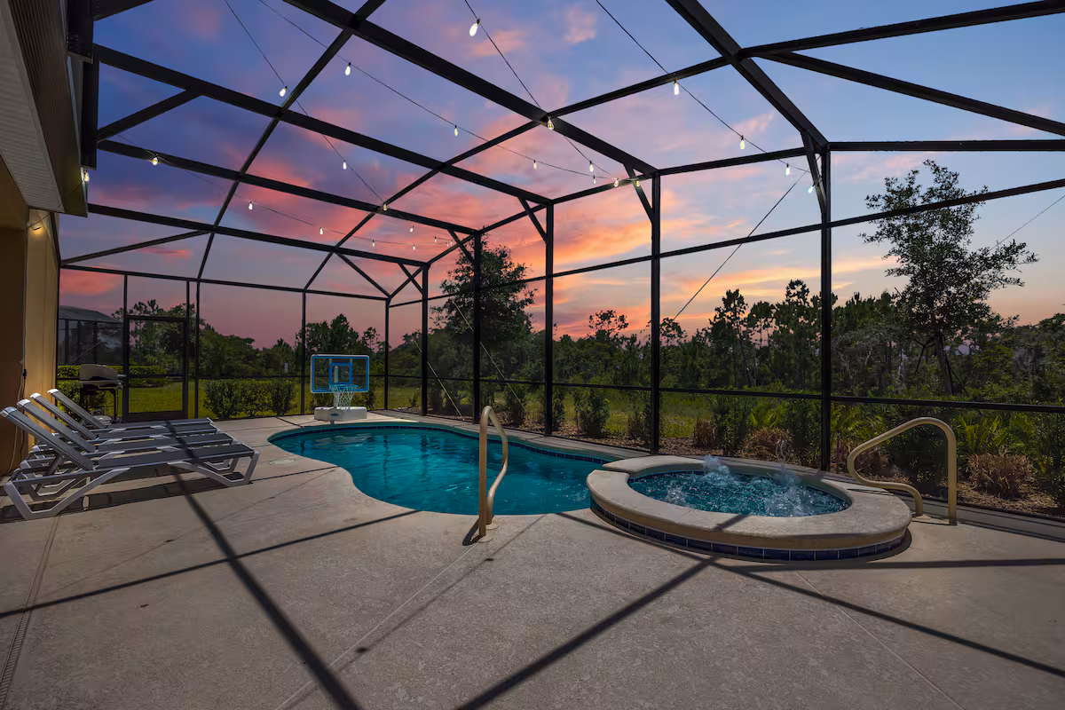 Screened pool area with lounge chairs, basketball hoop, and hot tub at sunset.