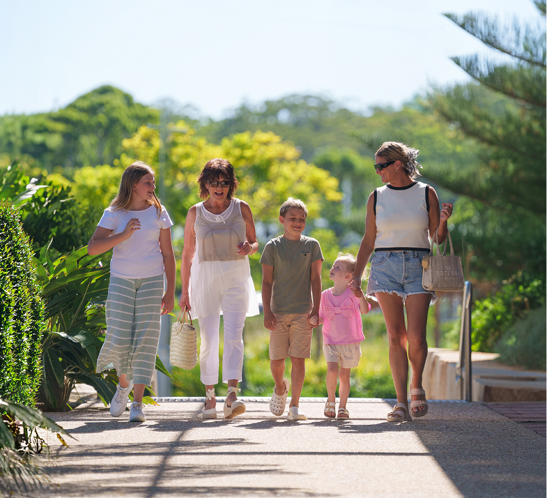 Group of five people, two women and three children, walking outdoors on a sunny day.