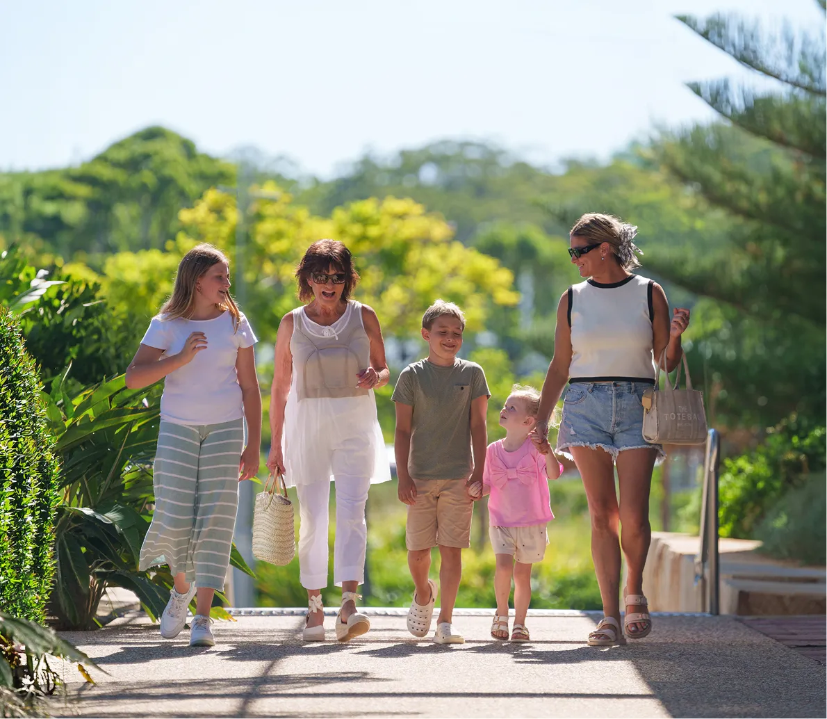 Five people walking outdoors on a sunny day surrounded by greenery, including two children and three women.