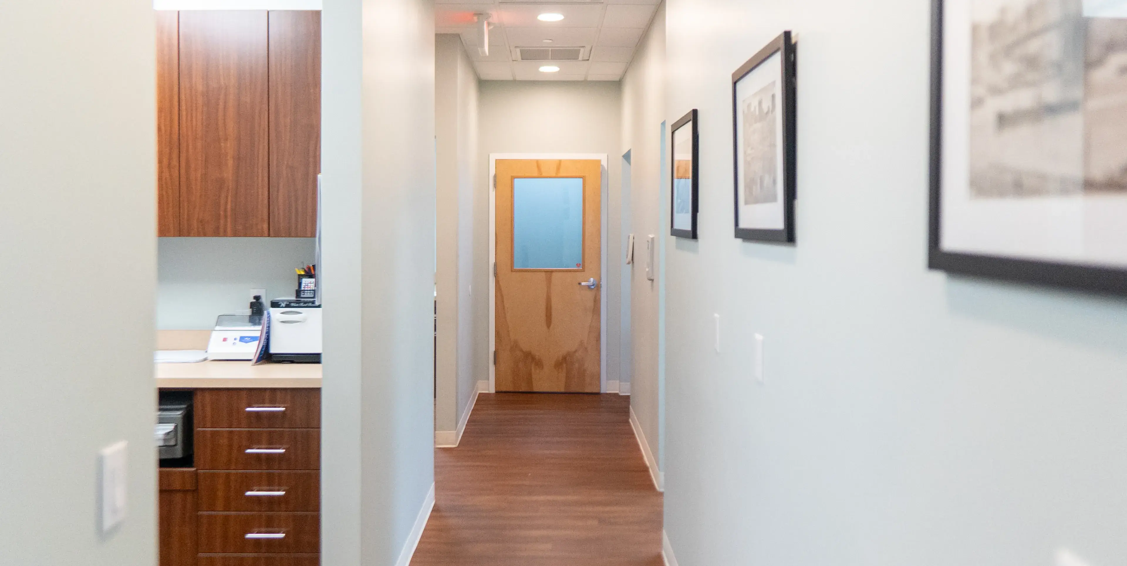 A hallway in an office with framed pictures on the wall and a wooden door at the end.