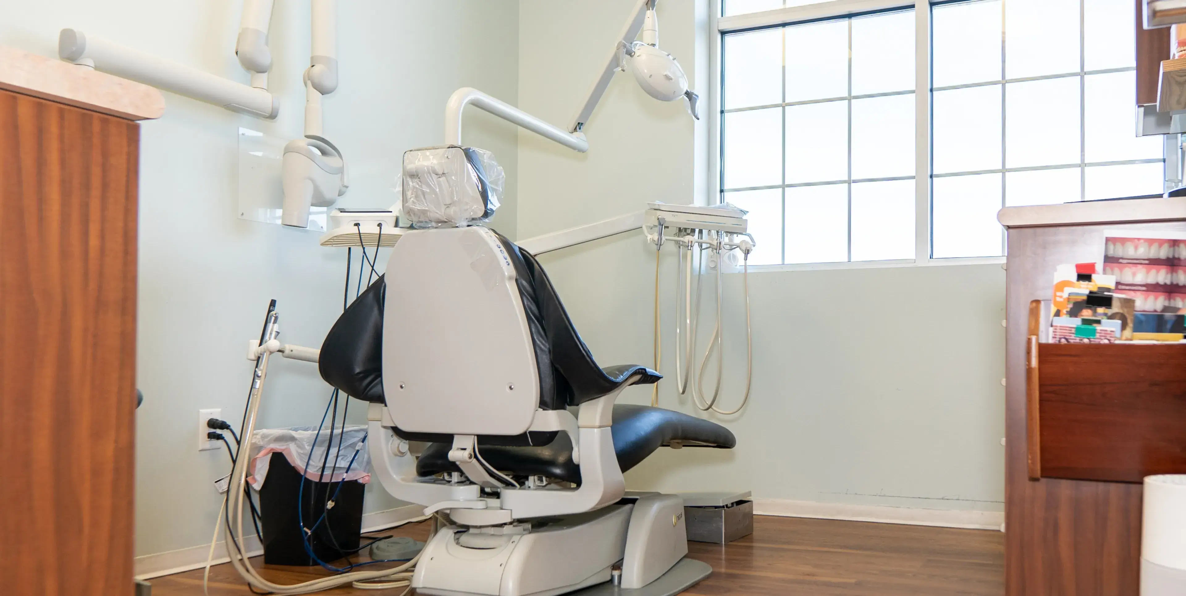An empty dentist chair in a clean clinic room, facing a frosted window.