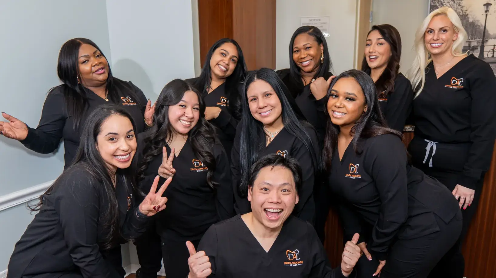 A group of smiling people in black uniforms pose together, making peace signs and thumbs up.